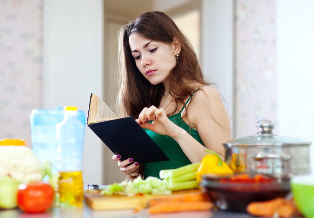 A woman writing a weekly meal plan in a notebook surrounded by vegetables, focusing on foods that have high fiber.