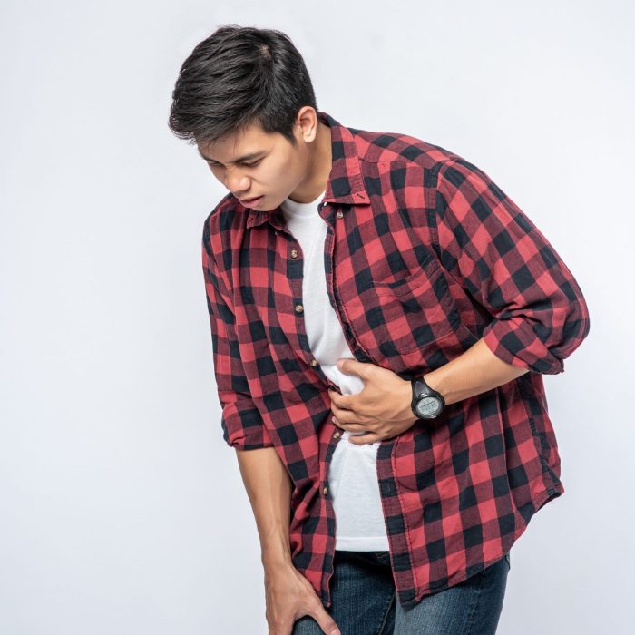 A man stands with a stomachache and puts his hand on his stomach.